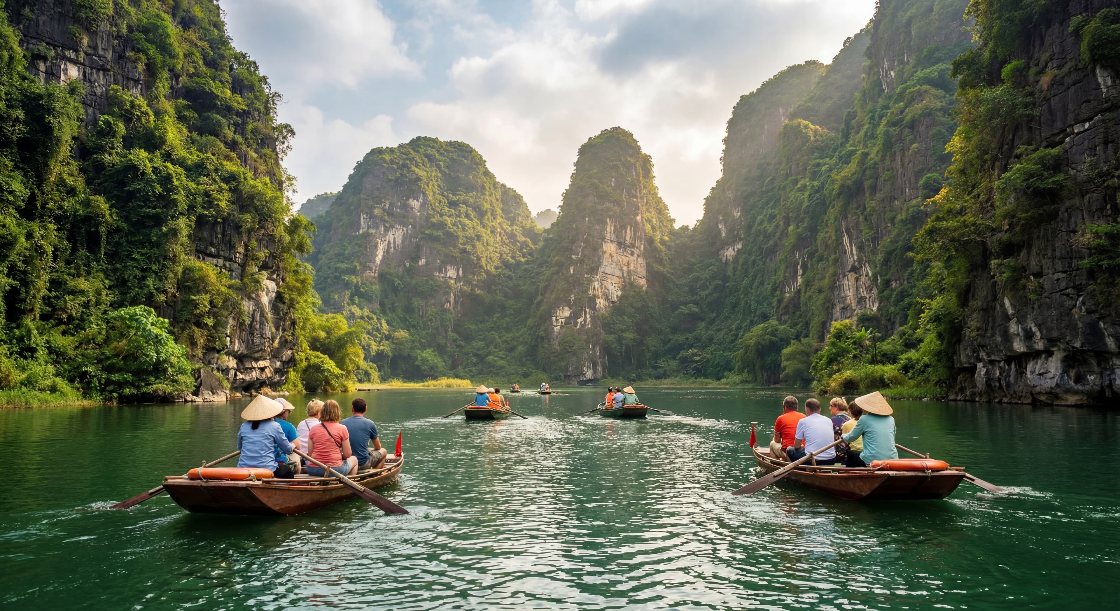 Tourists on small wooden boats paddling through the emerald green waters of Trang An scenic complex